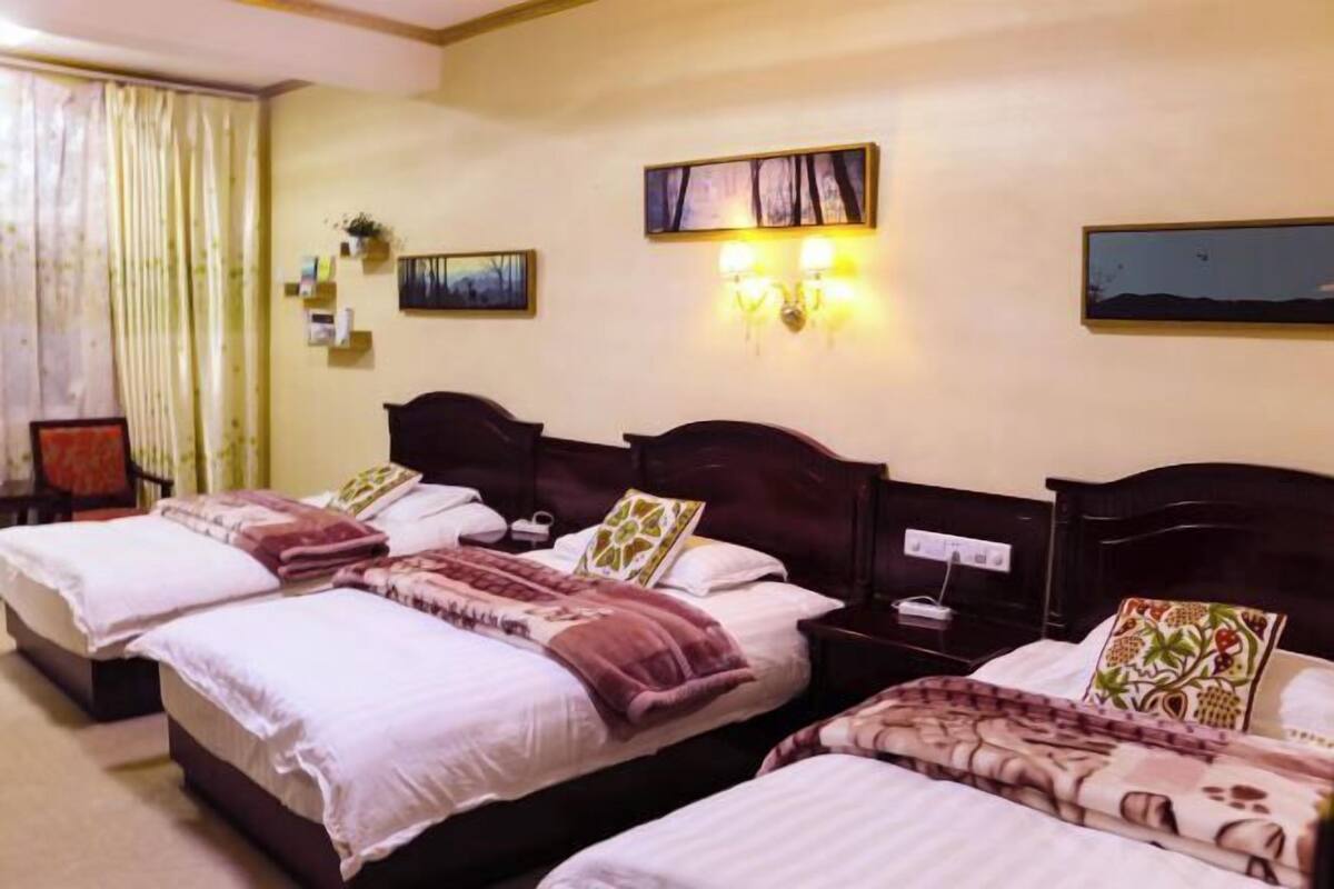 Habitación de hotel con tres camas, una mesita de noche, lámparas de pared y un cuadro.