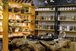 A rustic interior with wooden shelves filled with plants and jars, a wooden table with a kettle, and a rustic wall with storage containers. - Dzongsa Book bar Inn (Shangri-La)
