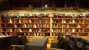 A cozy reading area with wooden bookshelves, a table, chairs, and a sofa. - Dzongsa Book bar Inn (Shangri-La)