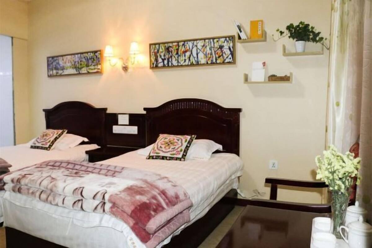 Habitación de hotel con dos camas, obra de arte colgada en la pared, repisas con objetos y una mesita con un florero.