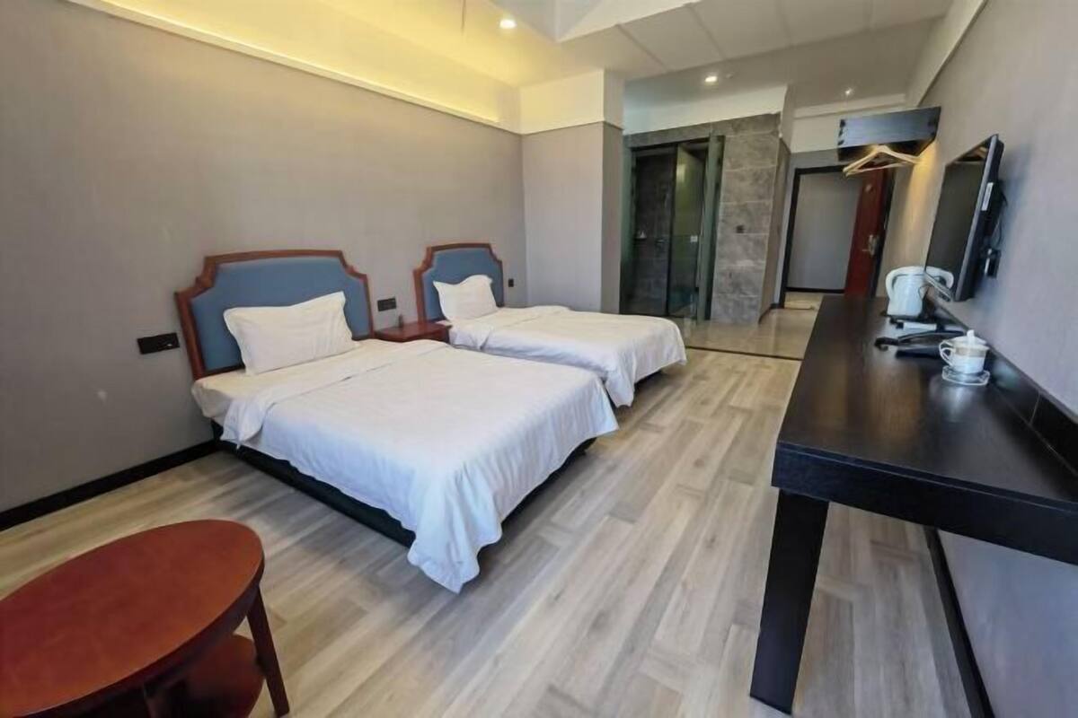 A hotel room with two beds, a desk, a chair, and a television.