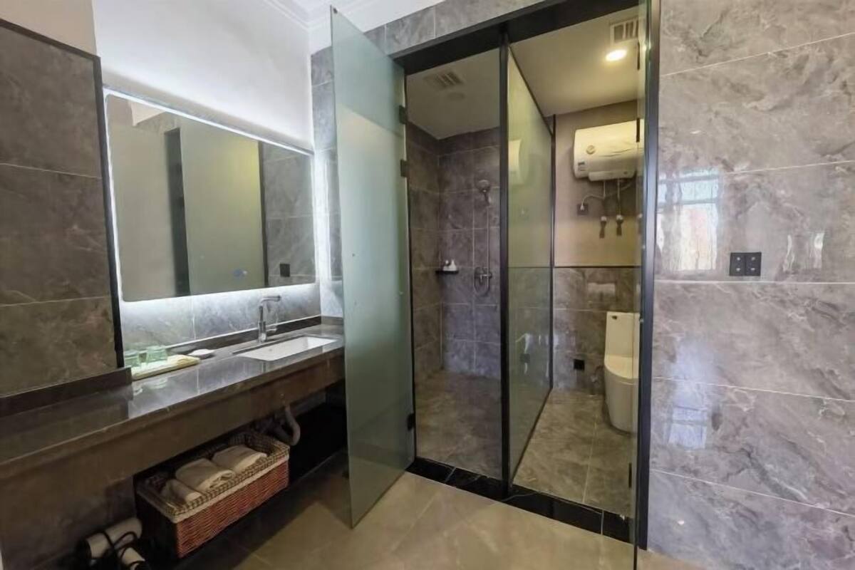 A modern bathroom with a glass shower enclosure, a large mirror, and a dark marble countertop.