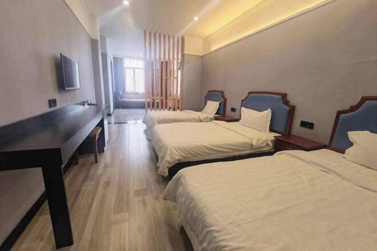 A hotel room with three beds, a TV, a bench, and a view of the outdoors.