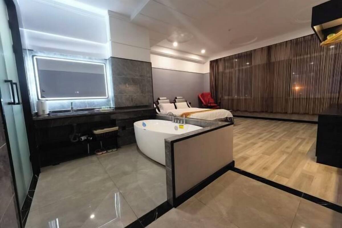 Una moderna camera d'albergo con un ampio letto, una zona salotto separata, un bagno con vasca e un grande specchio.