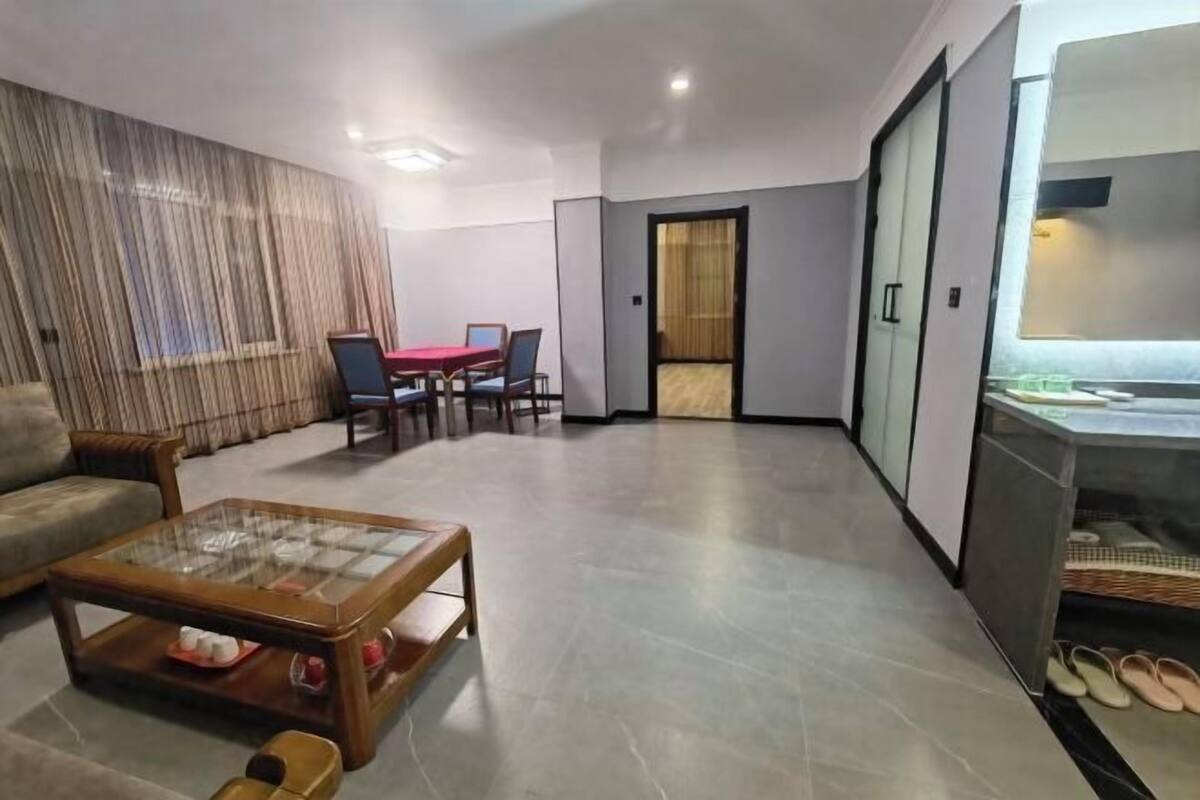 A modern living room with a glass coffee table, a sofa, a dining table with chairs, and a sliding door leading to another room.