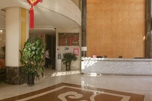 A hotel lobby with a reception desk, a large potted plant, and a patterned wall.