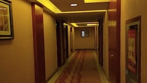Un couloir d’hôtel avec un tapis à motifs, des portes en bois et des œuvres d’art encadrées accrochées aux murs.