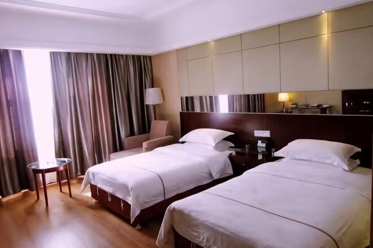 Habitación de hotel con dos camas, un escritorio, una silla, una lámpara y un ventanal grande con cortinas.