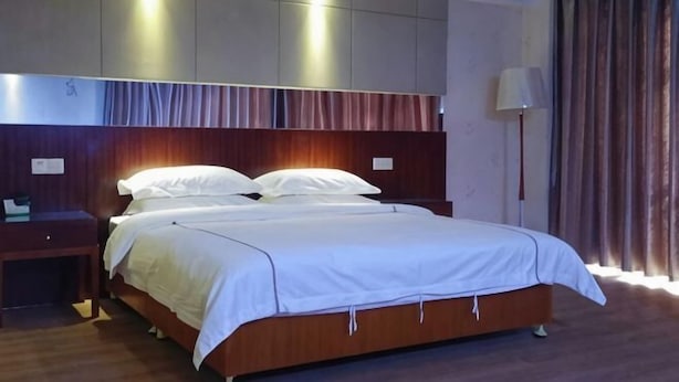 Une chambre d’hôtel avec un grand lit, une table de chevet, une lampe et une vue sur l’extérieur à travers les rideaux.