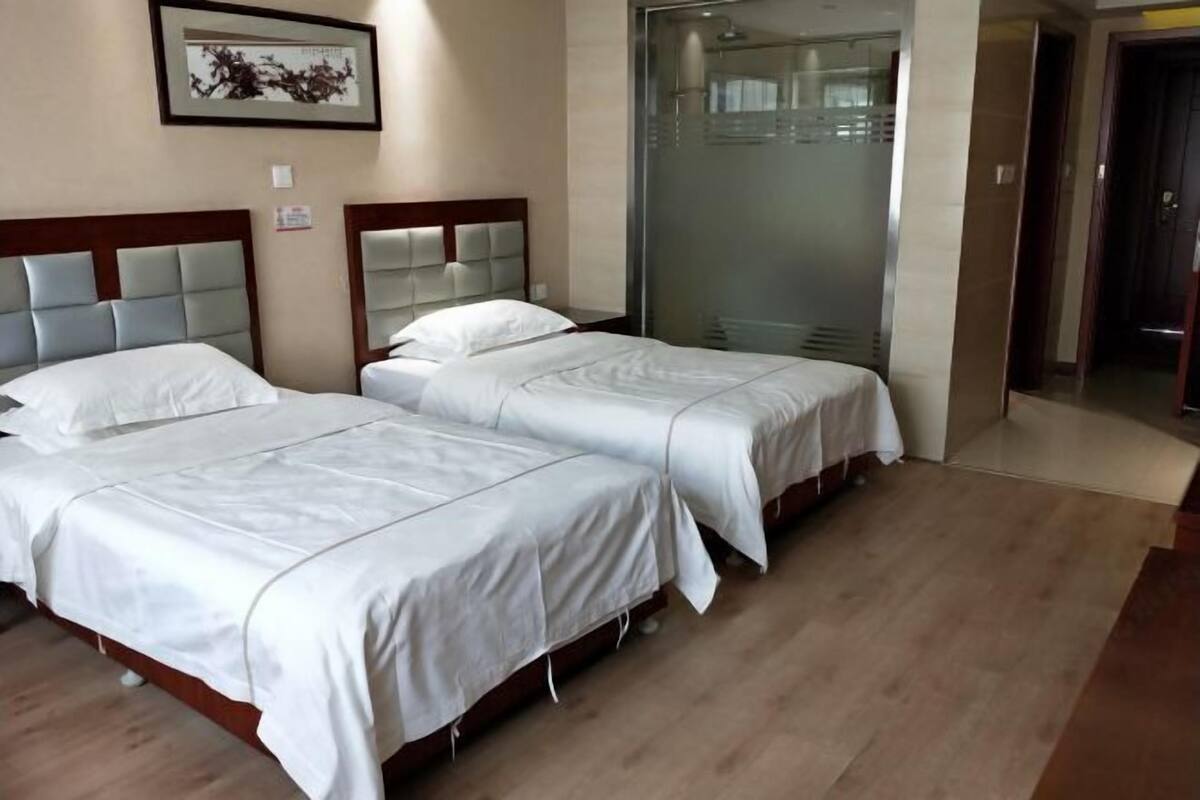 Habitación de hotel con dos camas, un espejo grande y una puerta corrediza de vidrio que da a una zona de ducha.