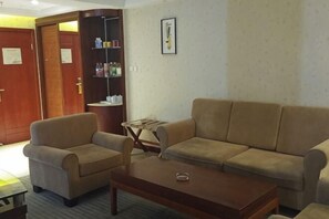 Ein Hotelzimmer mit einem beigefarbenen Sofa, einem Holztisch und einem Bücherregal.