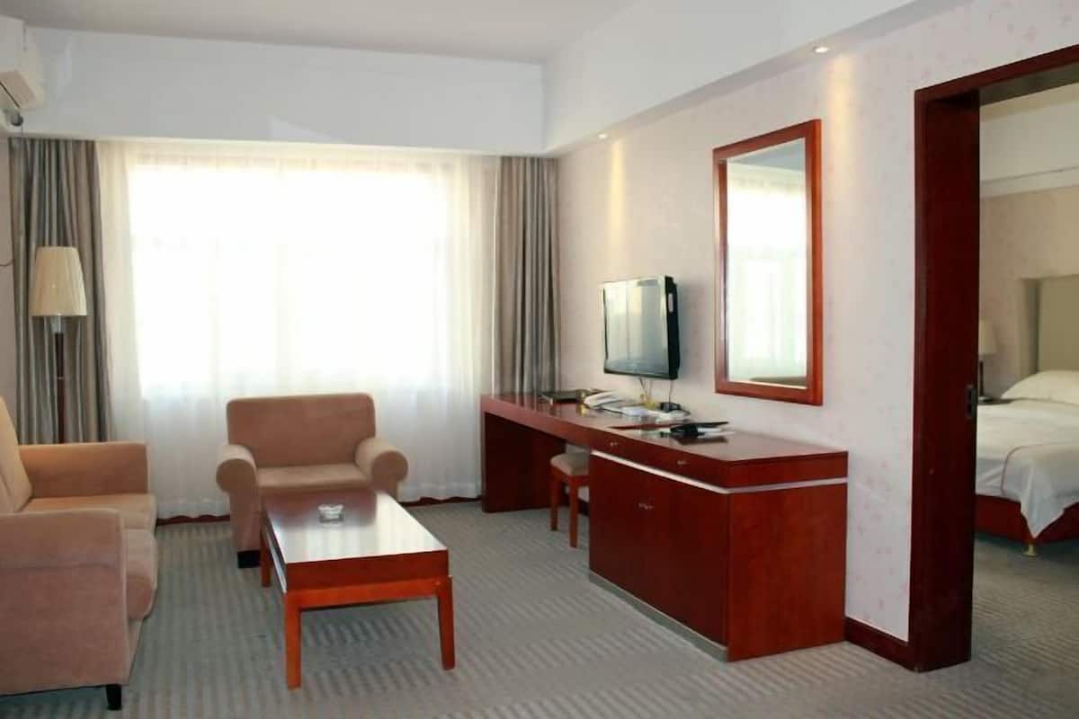 Habitación de hotel con cama, escritorio con televisor, una silla, un sofá y una mesita.