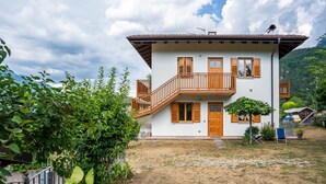 A two-story house with a balcony, a small garden, and a mountain backdrop.