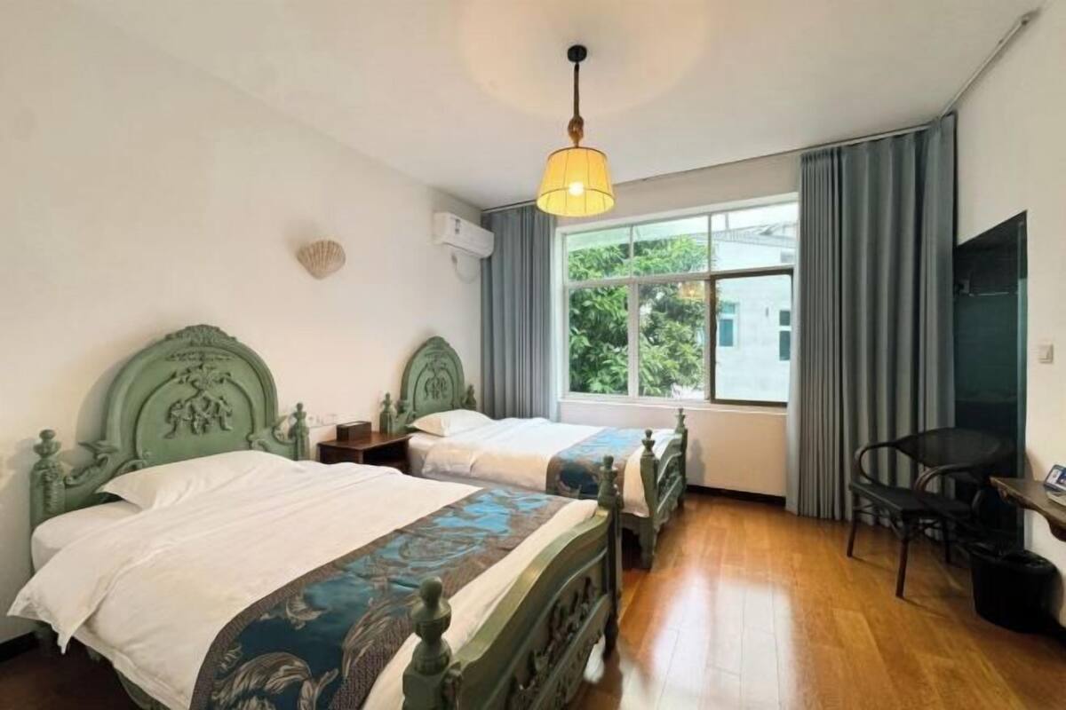 Una habitación con dos camas, una ventana con cortinas, una silla y una lámpara colgante.