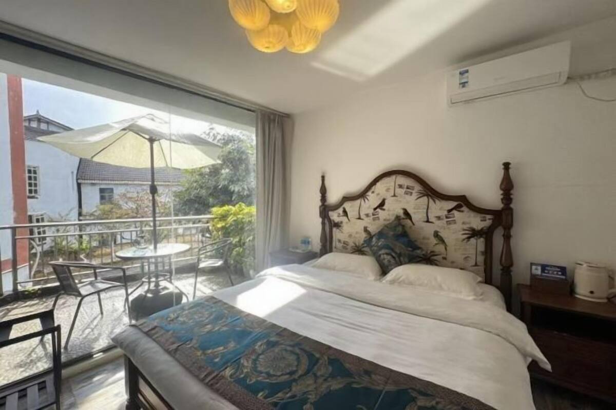 Un dormitorio con una cama grande, cabecera de madera con detalles artísticos, una mesita de noche pequeña y vistas al balcón exterior.