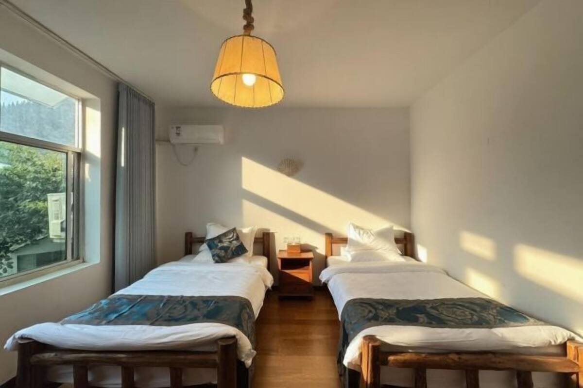Una habitación con dos camas, una lámpara colgante, un ventanal y aire acondicionado instalado en la pared.