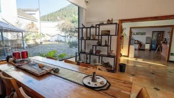Una mesa de comedor de madera con sillas, un estante con adornos, y vistas a un jardín y un edificio.