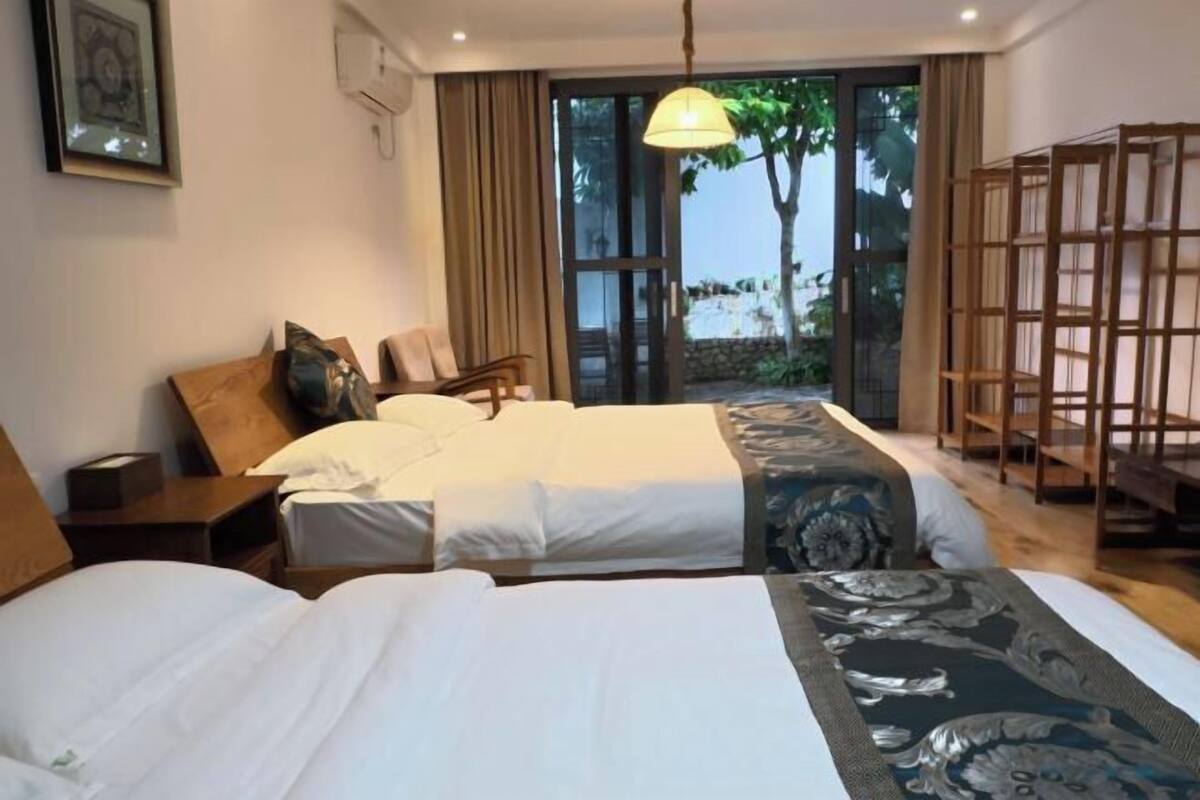 Habitación de hotel con dos camas, un ventanal grande y vistas a zonas verdes.