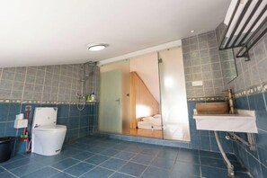 Un baño moderno con inodoro, ducha y puerta de vidrio que da a un dormitorio.