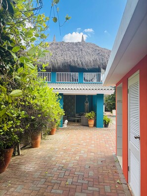A house with a thatched roof, a balcony, and a paved courtyard with potted plants.