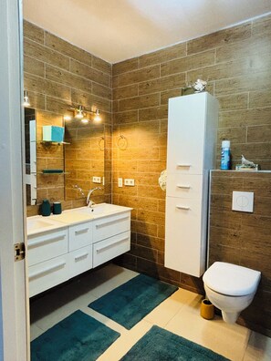 A bathroom with a white sink, mirror, and cabinet, wooden wall tiles, and a toilet.