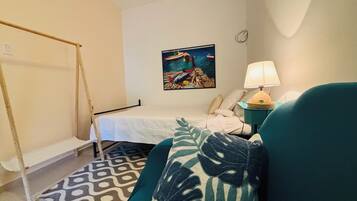 A bedroom with a bed, a green sofa, a patterned rug, a painting on the wall, and a lamp on a side table.