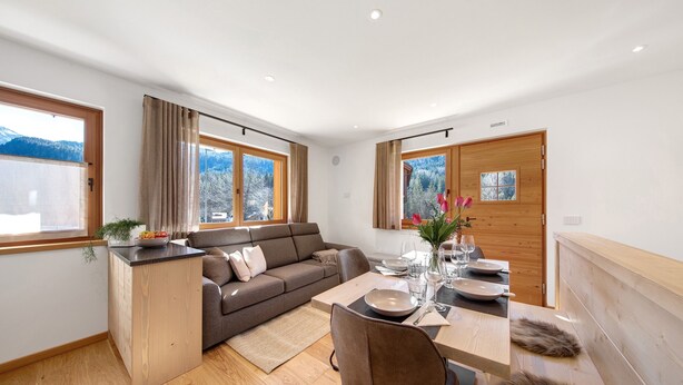 Een moderne woonkamer met een bank, eettafel en uitzicht op bergen door grote ramen.