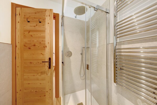Une porte en bois, une cabine de douche moderne, une porte en verre et un porte-serviettes métallique.