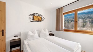 Een slaapkamer met een bed, nachtkastje, een kunstwerk aan de muur en een raam met uitzicht op bomen.
