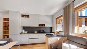 Een kleine keuken met een magnetron, spoelbak en kastjes, een eethoek met een tafel en stoelen, en een bank met kussens.