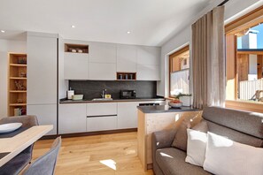 Een kleine keuken met een magnetron, spoelbak en kastjes, een eethoek met een tafel en stoelen, en een bank met kussens.