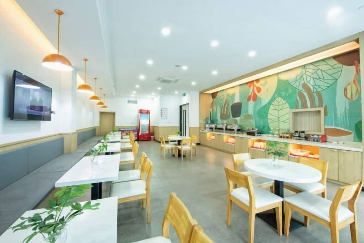 A modern restaurant with long communal tables, individual booths, and a colorful mural on the wall.