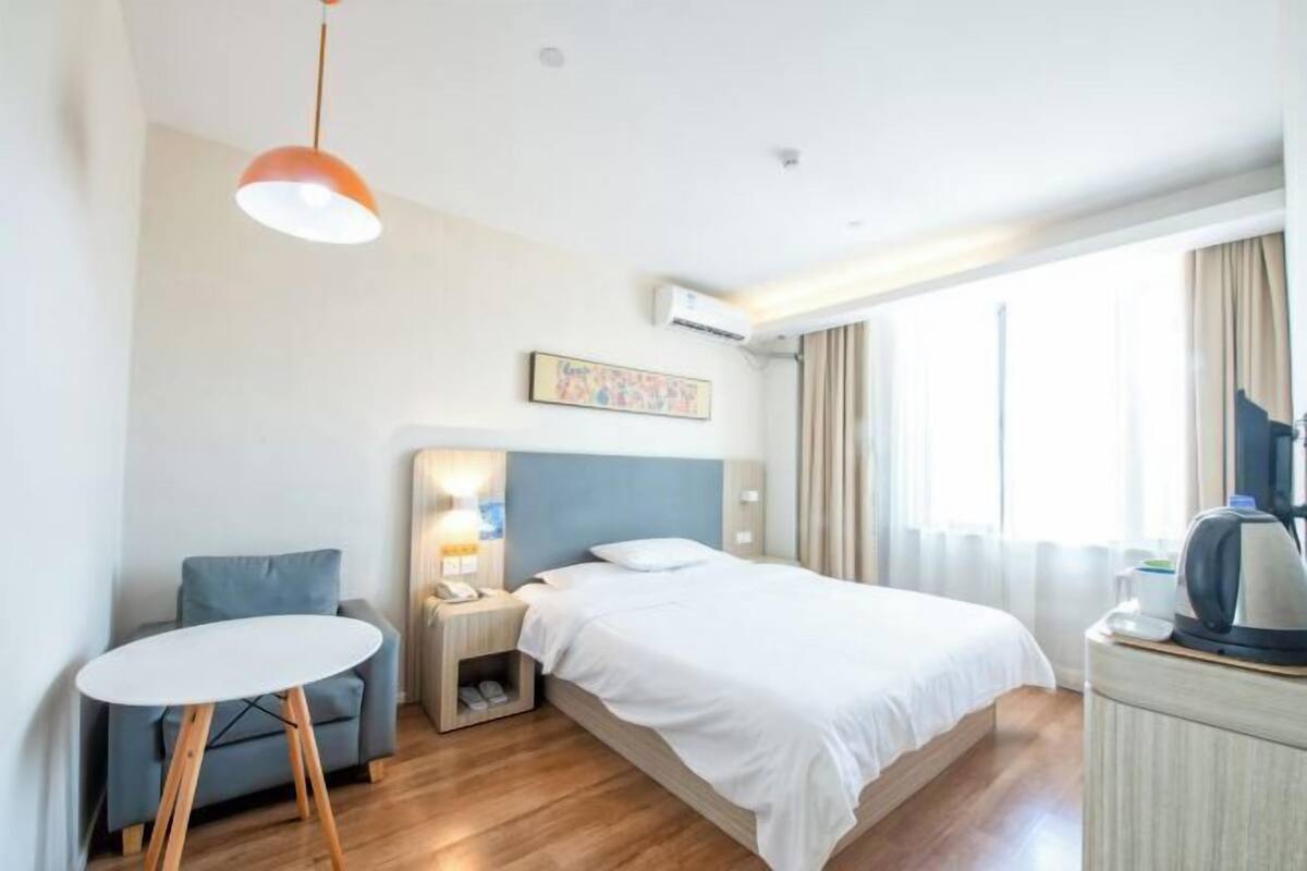 A hotel room with a bed, a desk, a chair, a round table, a coffee machine, and a window with curtains.