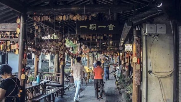 A covered outdoor area with wooden tables and benches, hanging decorations, and a sign with Chinese characters. - Wanting Hotel (Shanghai Xinchang ancient town store) (Shanghai)