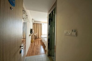 A hotel room with a wooden floor, a bed, a desk, and a chair. There is a door on the left and a window with curtains. - Wanting Hotel (Shanghai Xinchang ancient town store) (Shanghai)