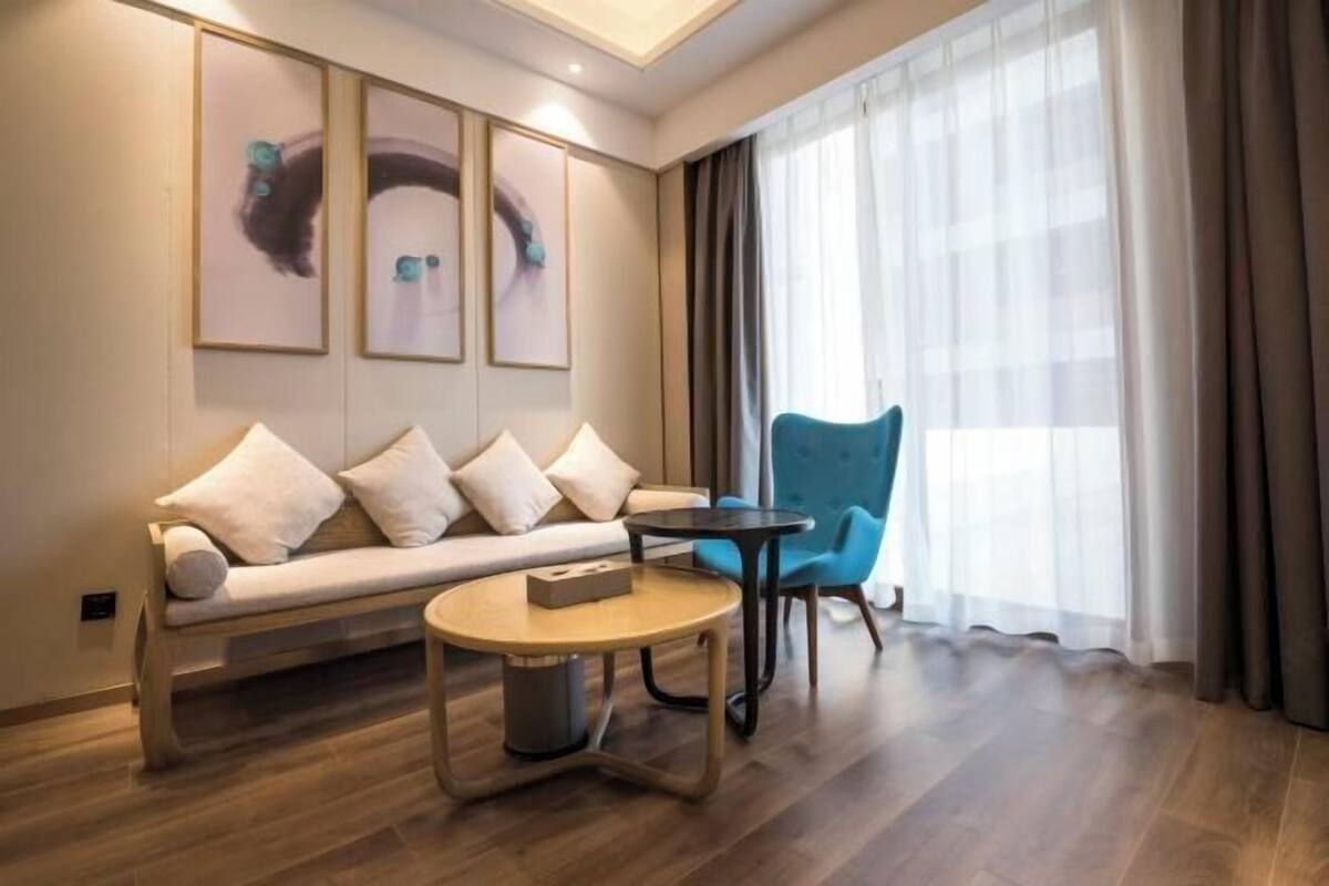 A modern hotel room with a sofa, a round coffee table, a blue chair, and artwork on the wall.