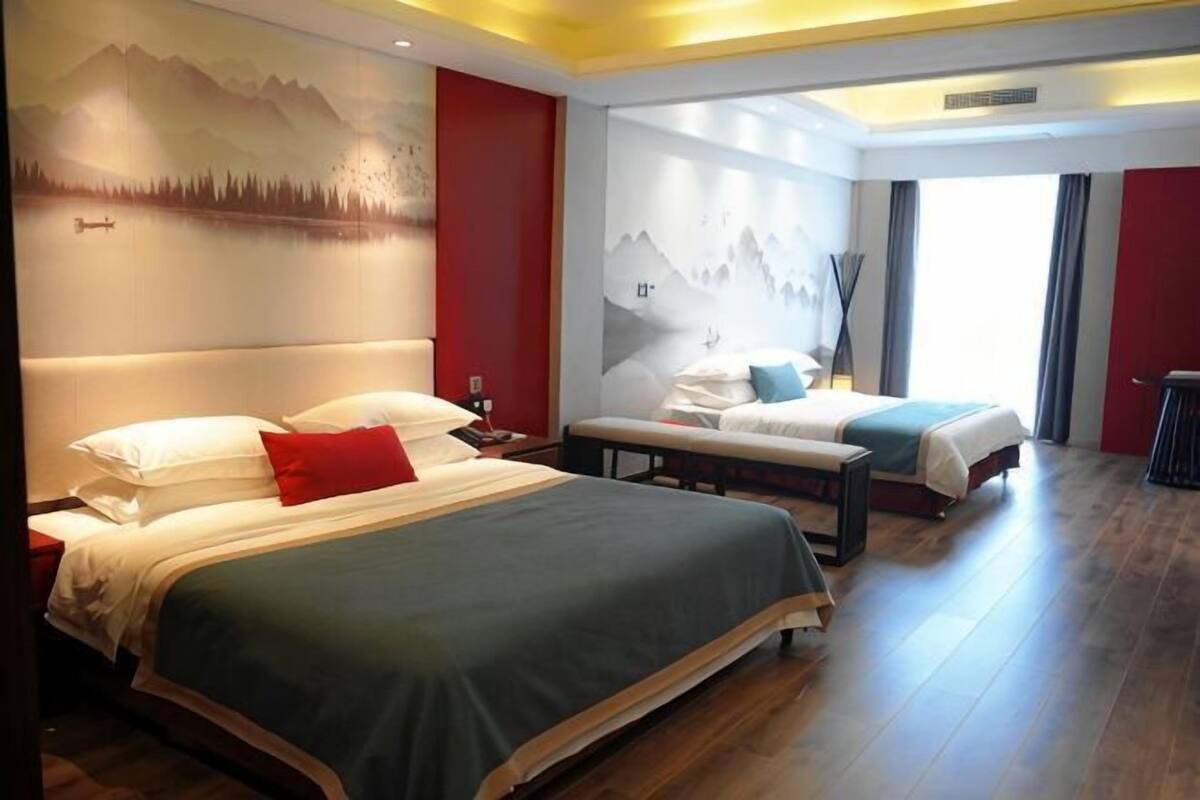 A hotel room with two beds, a large window, and a mountain mural on the wall.