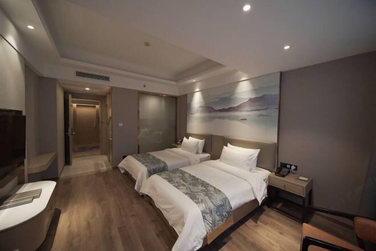 A hotel room with two beds, a desk, a chair, and a painting on the wall.