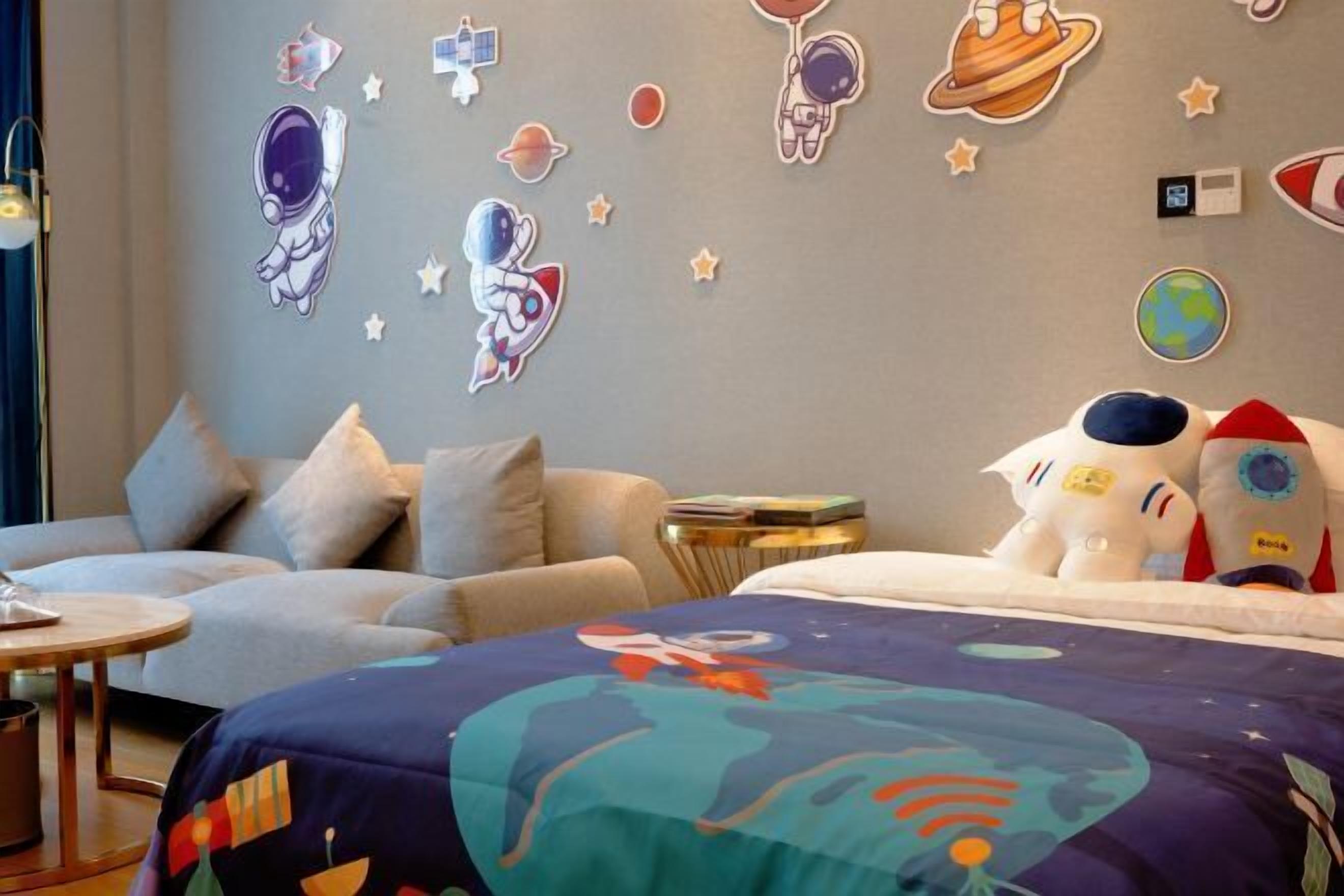 A room with a bed, two sofas, a small side table, and wall decorations including space-themed stickers and a globe.