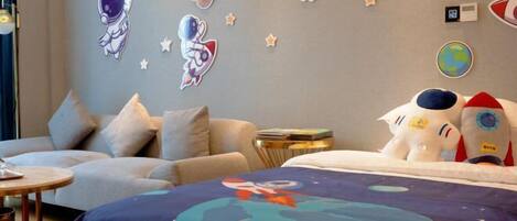 A room with a bed, two sofas, a small side table, and wall decorations including space-themed stickers and a globe.