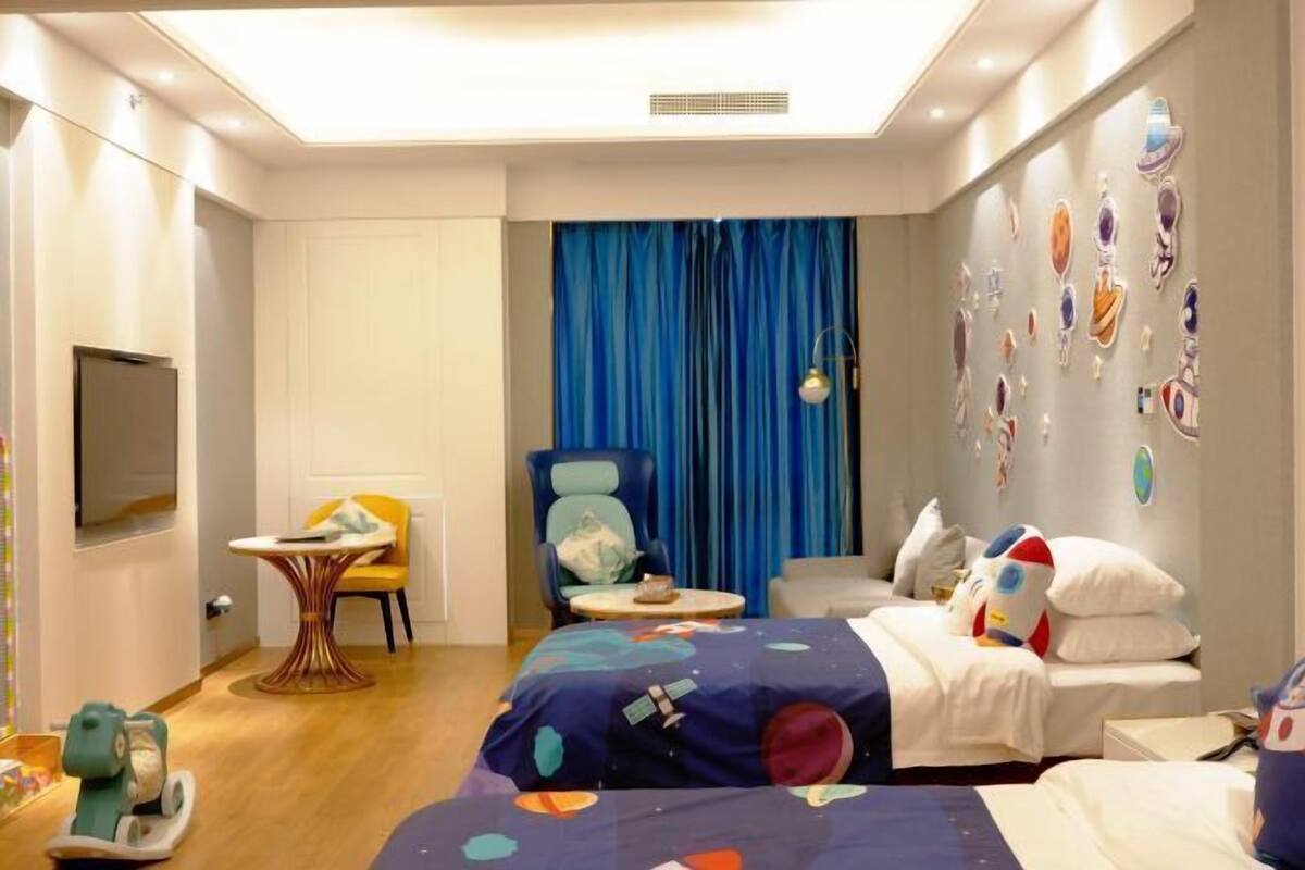 A hotel room with a bed, a desk, a chair, a TV, and a wall with decorative items.