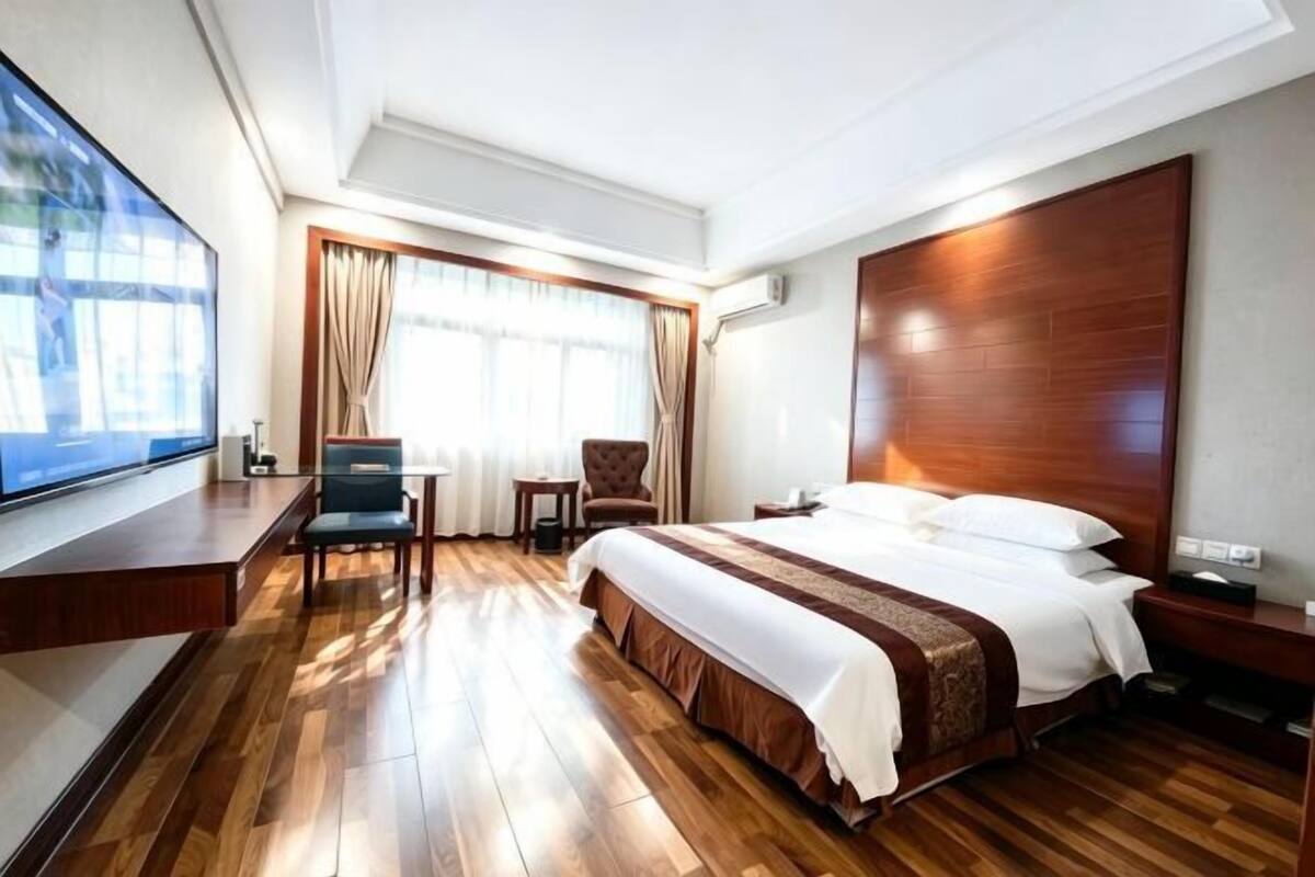 A hotel room with a large bed, a desk, a chair, and a TV.