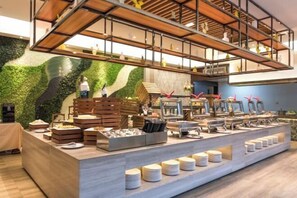 A buffet setup with various food items and a green wall backdrop. - Putian Golden Bay Hotel (Wanda Plaza Branch) (Putian)