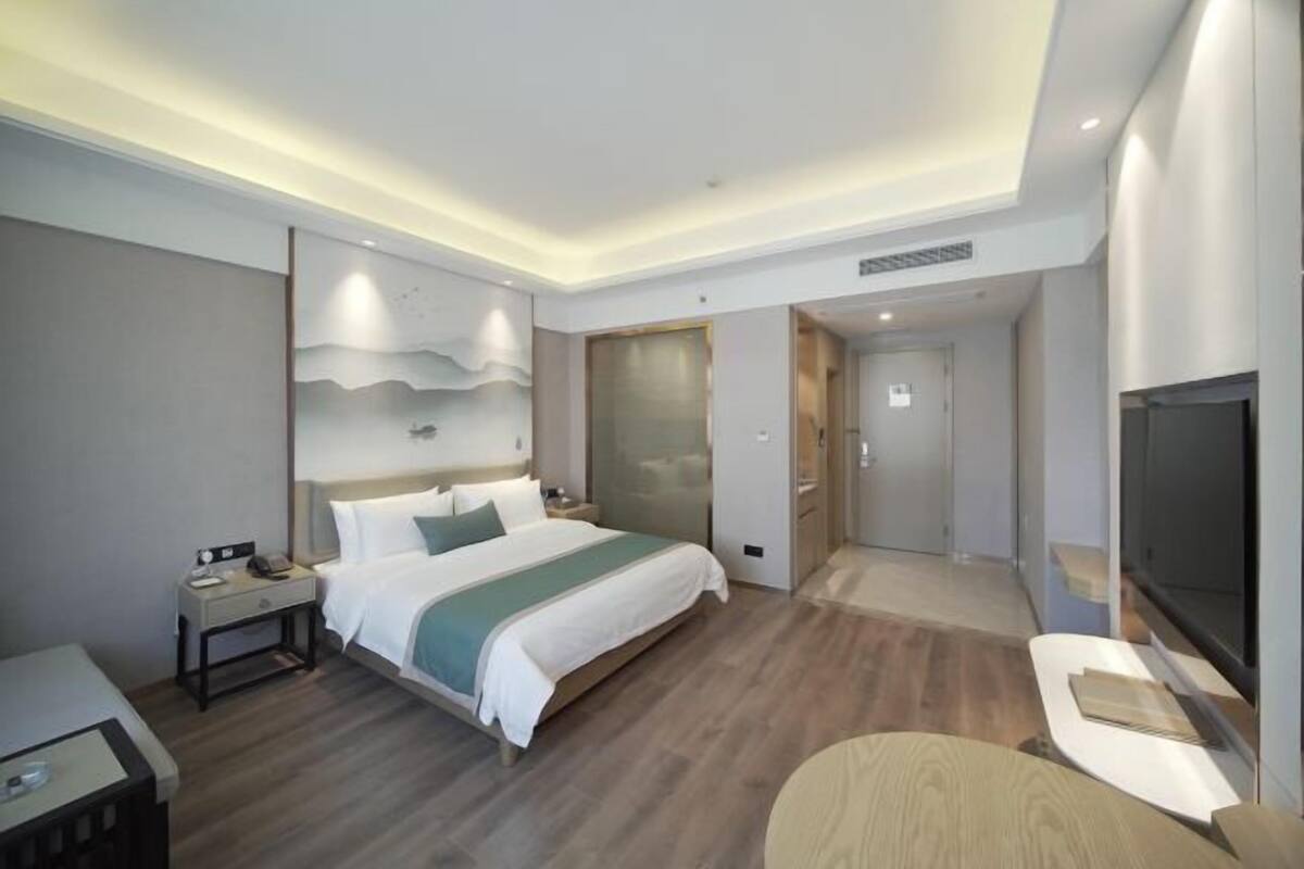 A modern hotel room with a large bed, bedside table, TV, and a walk-in closet.