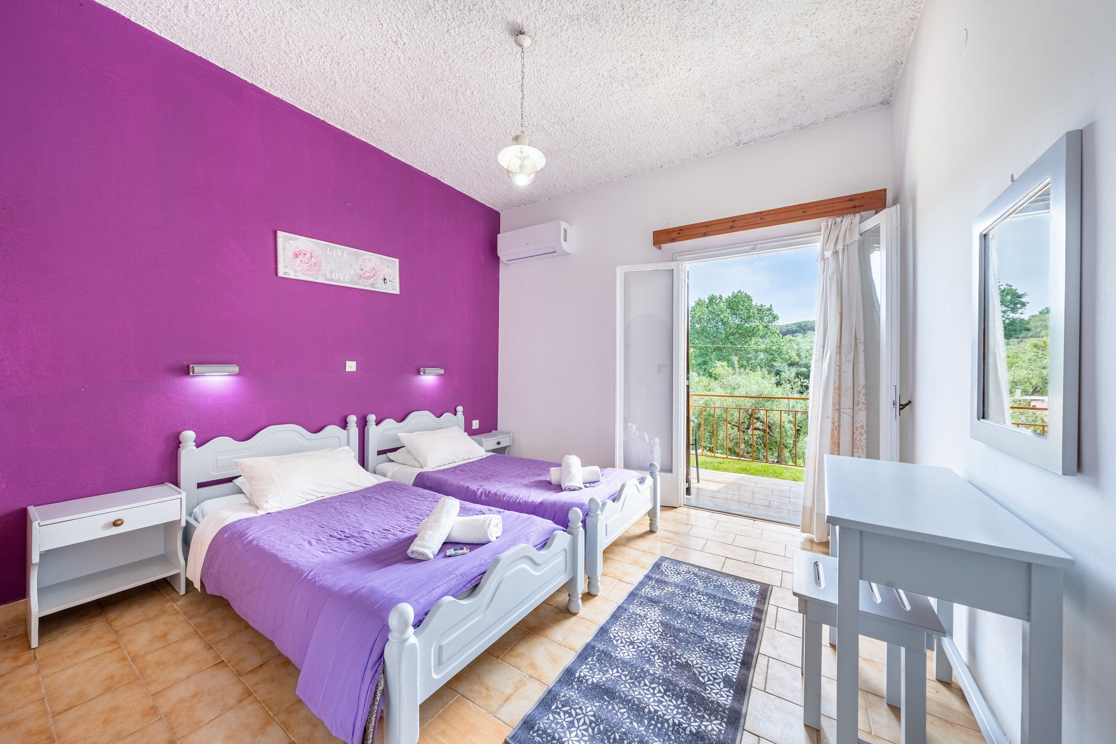 A bedroom with two beds, a desk, and a balcony with a view.