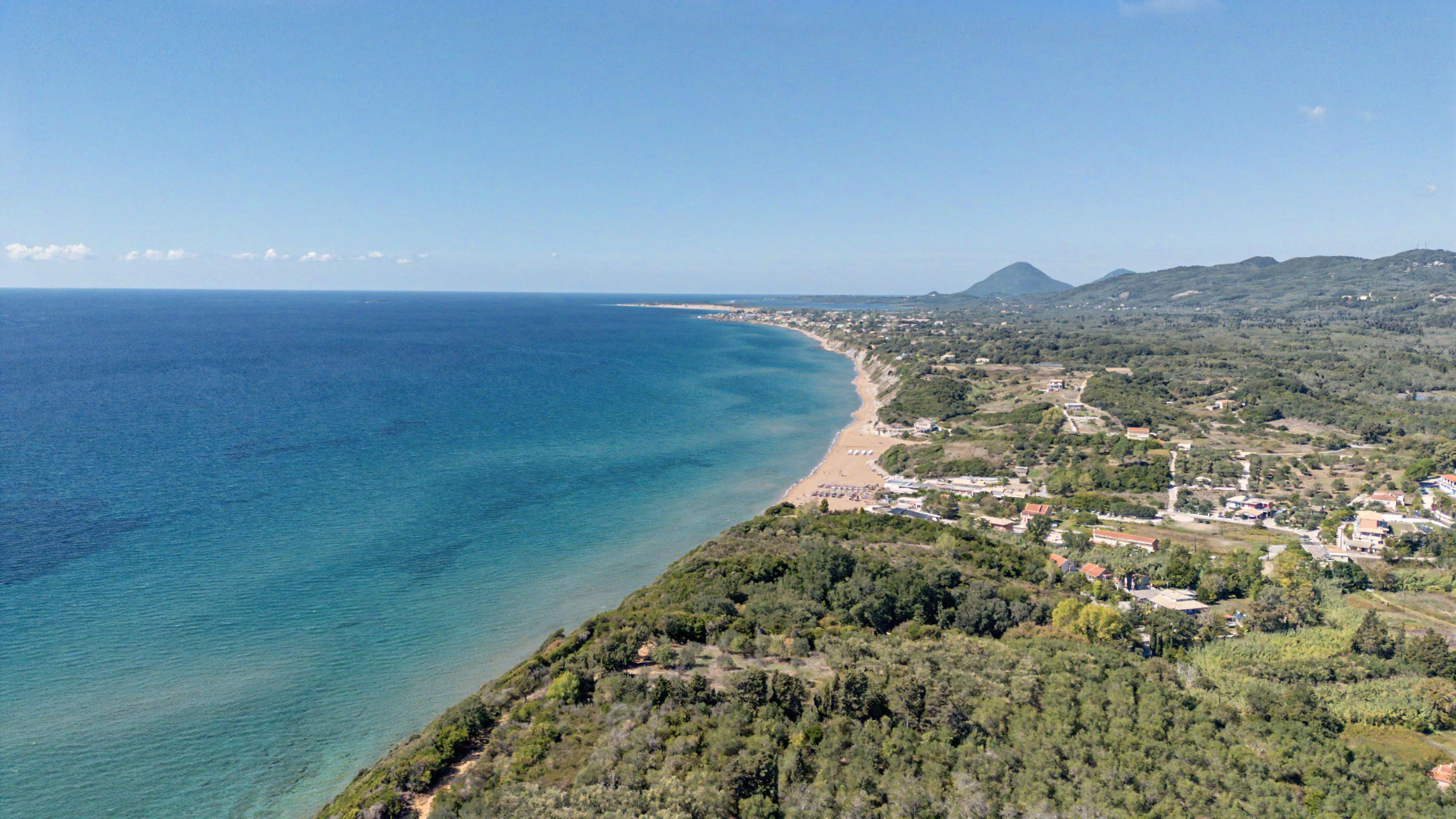 Una località costiera con spiaggia, edifici e colline sullo sfondo.