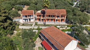 A two-story building with a red-tiled roof, multiple balconies, and a surrounding landscape with trees and vegetation. - Studio Apartment 'Maltas 6' with Shared Terrace, Wi-Fi and Air Conditioning (Corfu)