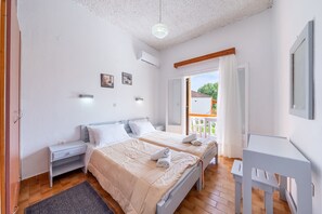 A bedroom with two beds, a desk, and a balcony.