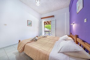 Un dormitorio con dos camas, cabecero de madera, techo blanco y vista a un balcón exterior.