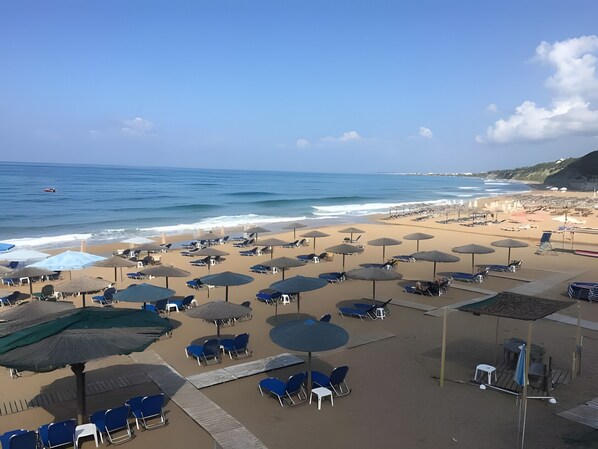 Una playa con sombrillas, sillas y vista al océano.